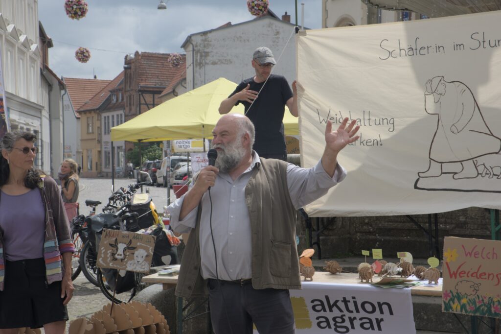 Jörn Mothes spricht vor Banner "Schäfer:in im Sturm" (Foto: M. Krack)